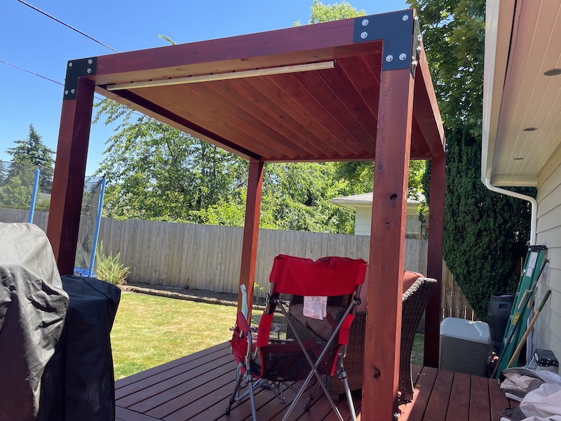 Picture of a cedar pergola with opening and closing roof slats, finished in a red sealant.